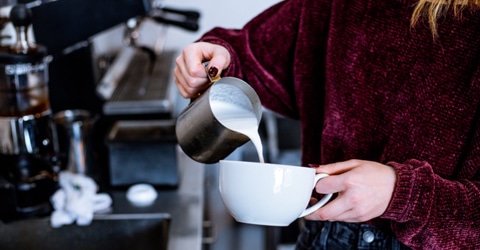 persona vertiendo leche al vapor en una taza